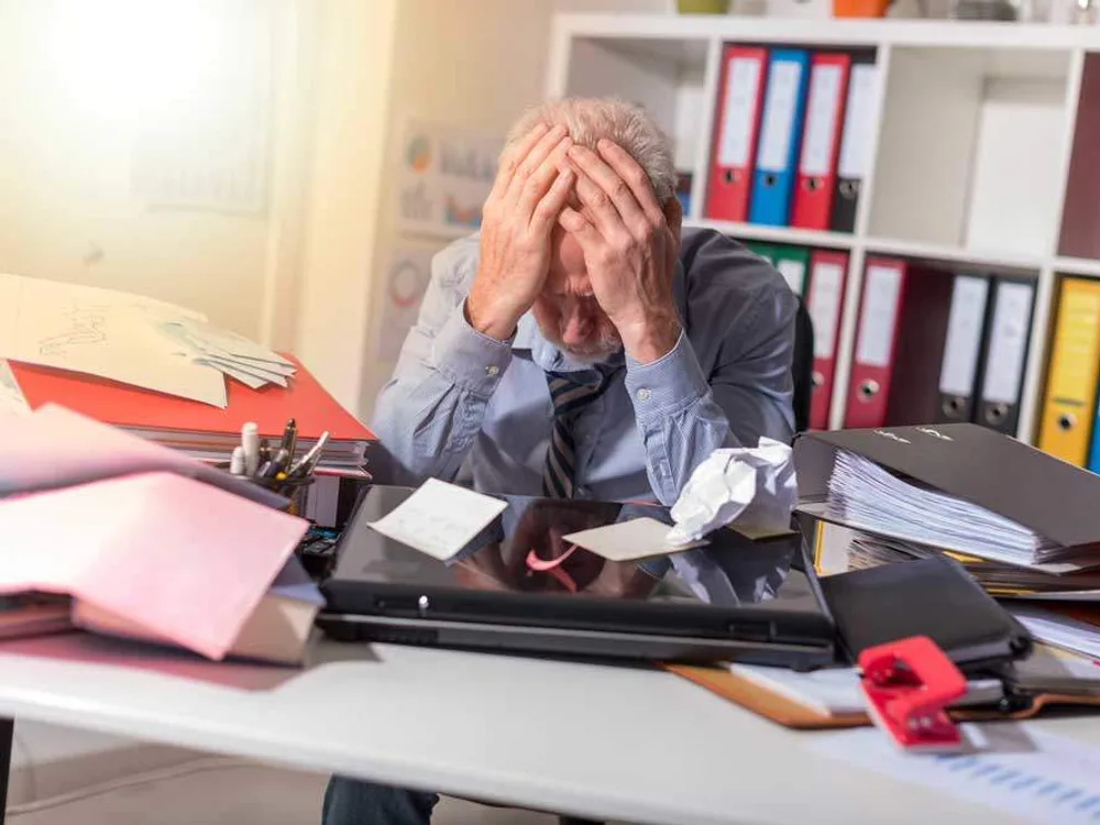 Un dirigeant débordé devant un bureau couvert de dossiers et de documents